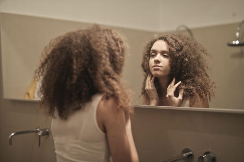 Girl looking at herself in the mirror and smiling at herself.