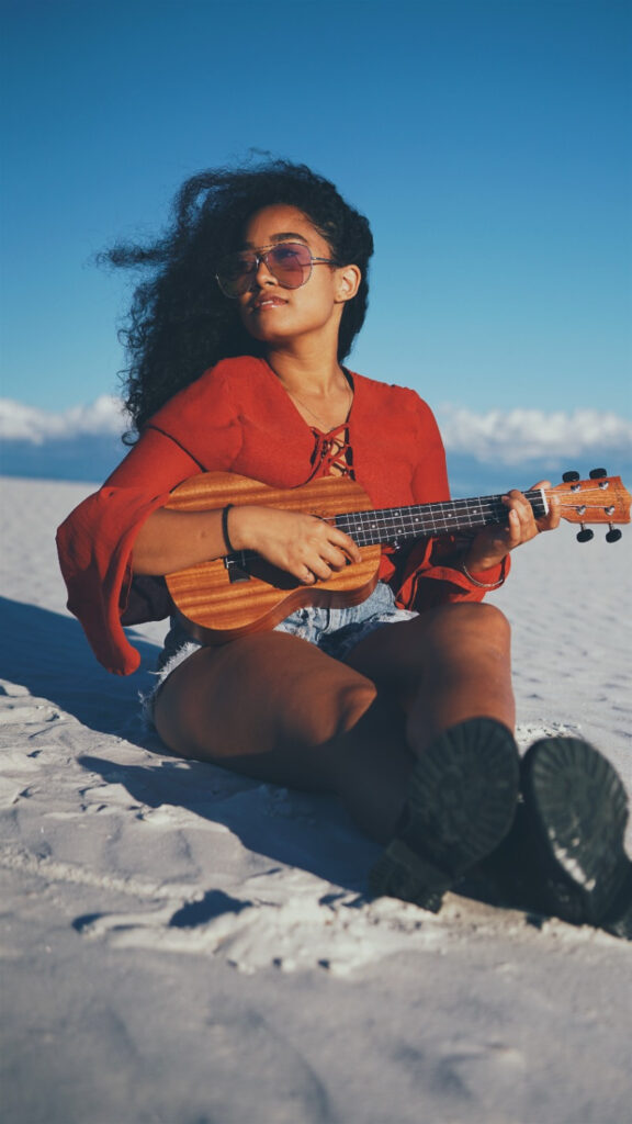 Woman playing a guitar while sitting in the sand at the beach.