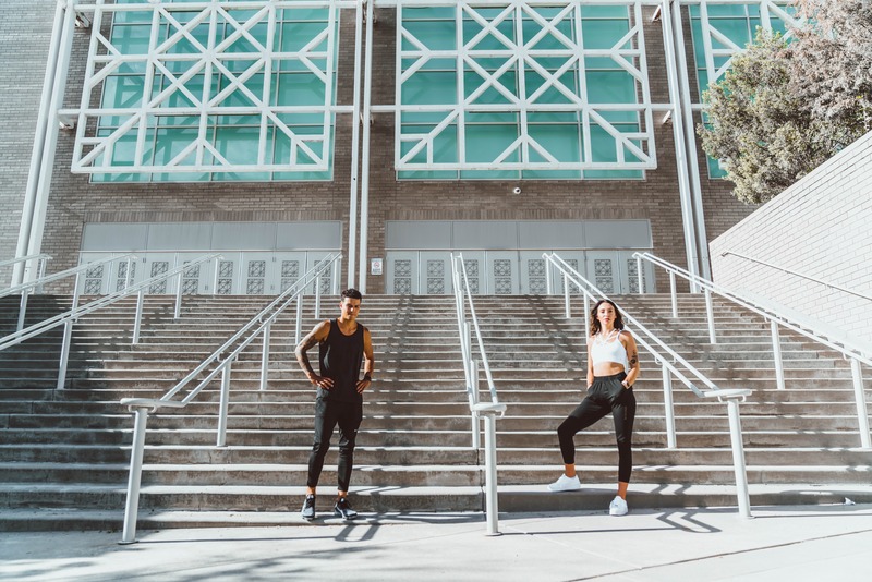 Man and woman posing on steps with workout outfits on.