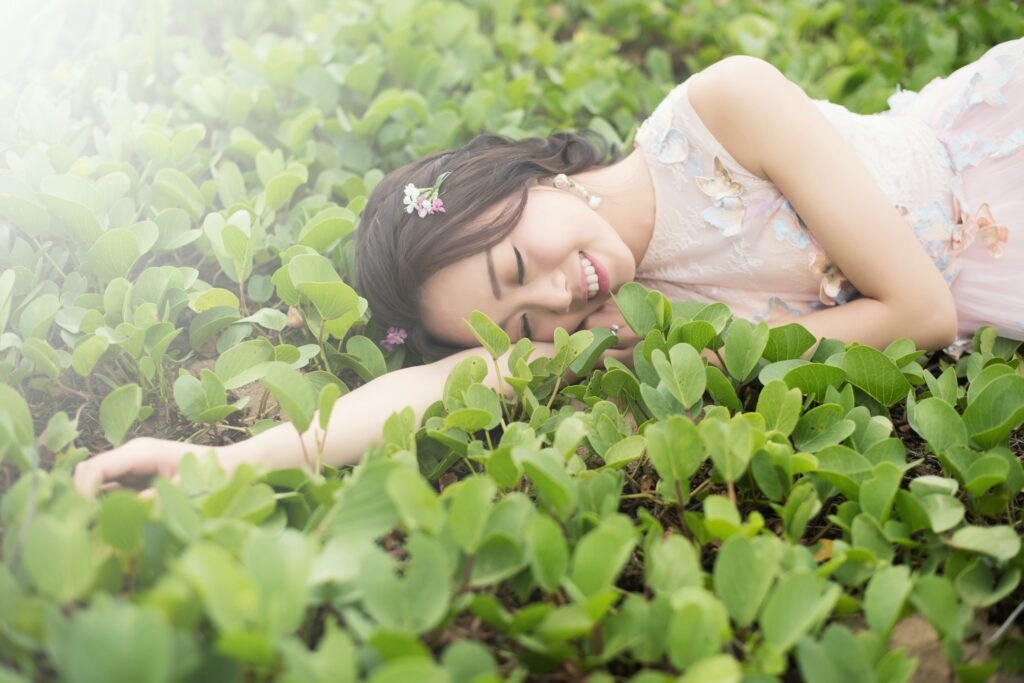 Girl laying in grass and smiling with her eyes closed. She is enjoying the nature around her and embracing her true beauty.
